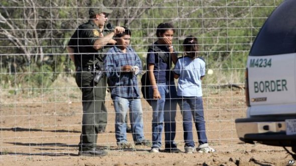 A Border Patrol agent stands on a ranch fence line with children taken into custody in South Texas brush country north of Laredo, Texas.  (FILE - VOAnews)