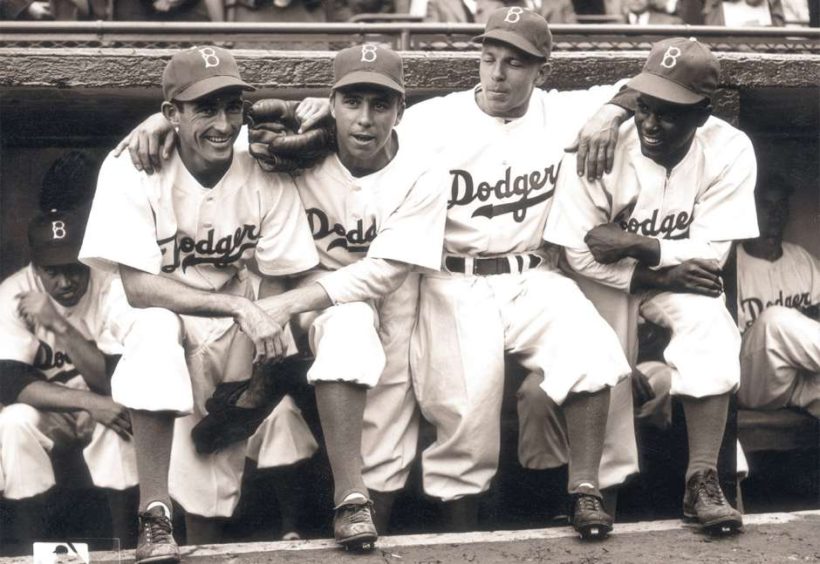 Robinson (right) poses with teammates (L-R) Johnny ‘Spider’ Jorgensen, Harold ‘Pee Wee’ Reese and Eddie Stanky on the steps of the Dodgers dugout during Robinson’s first official regular-season game on Opening Day.  (Photo File/Hulton Archive) 