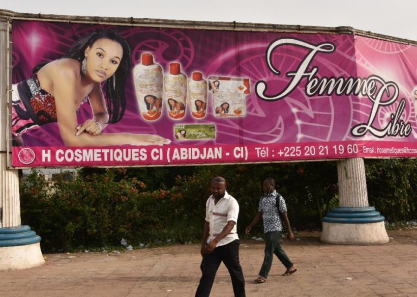 Two men walk under a giant advertisement for skin-lightening products in Abidjan on May 2, 2015 (AFP Photo/Sia Kambou)