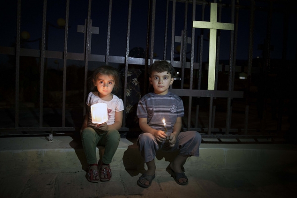 Two young Assyrians sit next to the fence with a Cross. They fled with their families from Islamic State's held Mosul to Koysinjaq, Iraqi Kurdistan.