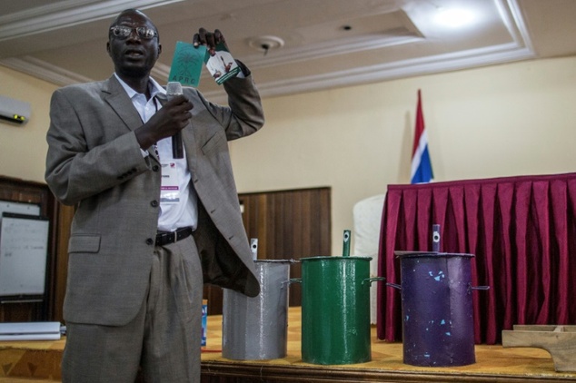 An IEC (Independent Electoral Commission) official shows an electoral document of incumbent president Yahya Jammeh next to the ballot boxes with the three parties colours on November 28, 2016.
